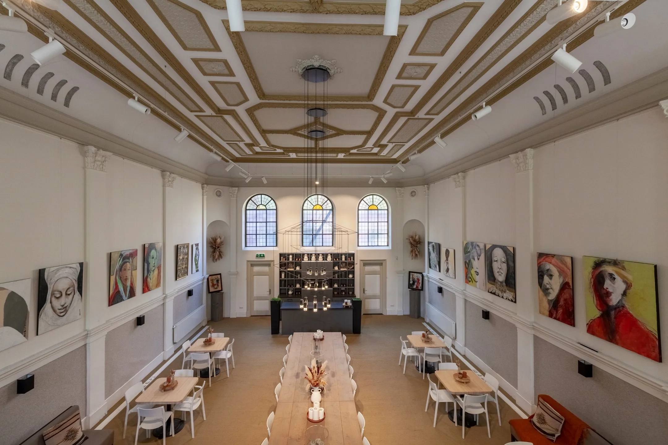 The main hall inside Peperstraat 20, with long tables, arched windows and paintings along the walls.